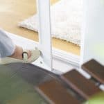 Person, die eine Tür mit einem Fuß öffnet, um auf einen Insektenschutz-Türöffner zu drücken, der unten an der Tür angebracht ist.