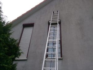 Eine Metallleiter lehnt an einem zweistöckigen Haus mit einem geschlossenen Fenster auf der linken Seite.