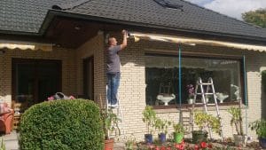 Mann auf einer Leiter repariert die Dachrinne eines Vorstadthauses.