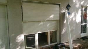 Teilweise angehobener Rollladen an einem Fenster eines Gebäudes mit Werkzeugen in der Nähe, was auf Wartungs- oder Reparaturarbeiten hindeutet.