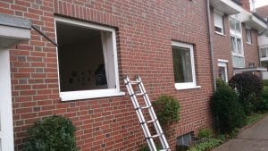 Eine an einem Gebäude angebrachte Metallleiter, die zu einem offenen Fenster an einer Backsteinfassade führt.