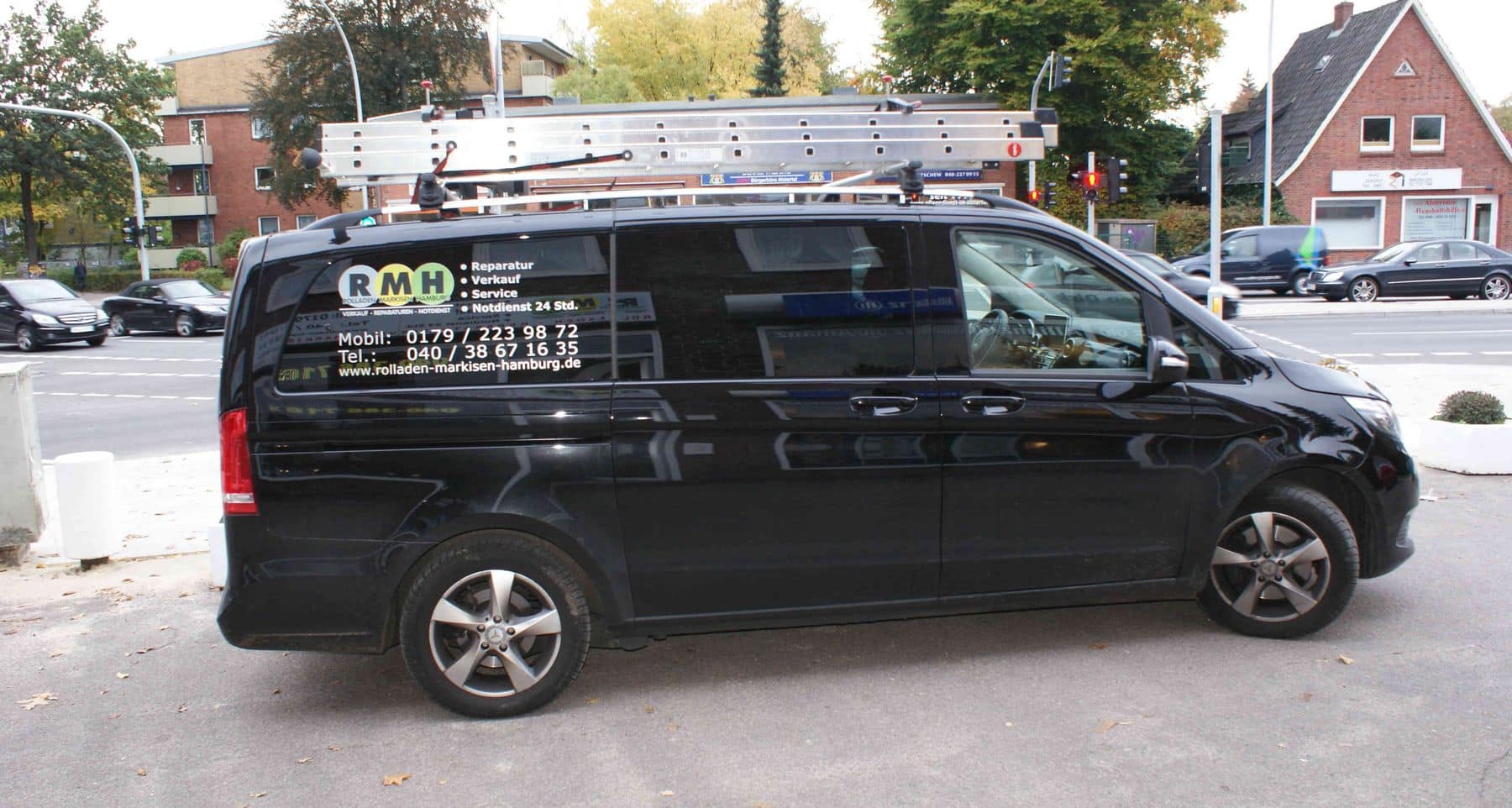 Ein am Straßenrand geparkter schwarzer Lieferwagen mit Leitern oben und Kontaktdaten des Unternehmens an der Seite.